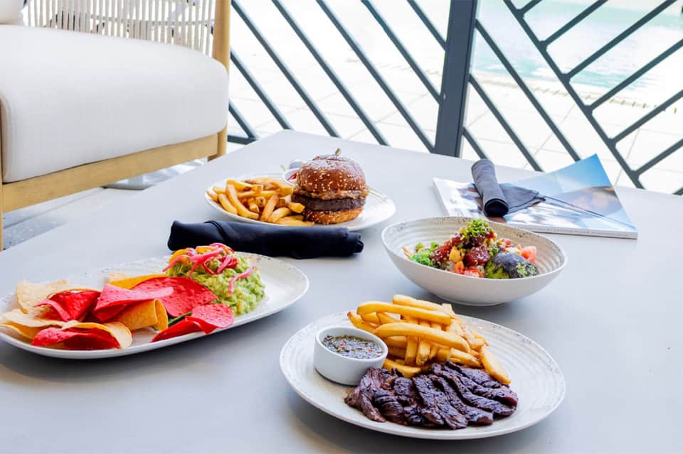 Beachfront dining table with burgers, salads, and fries overlooking the ocean