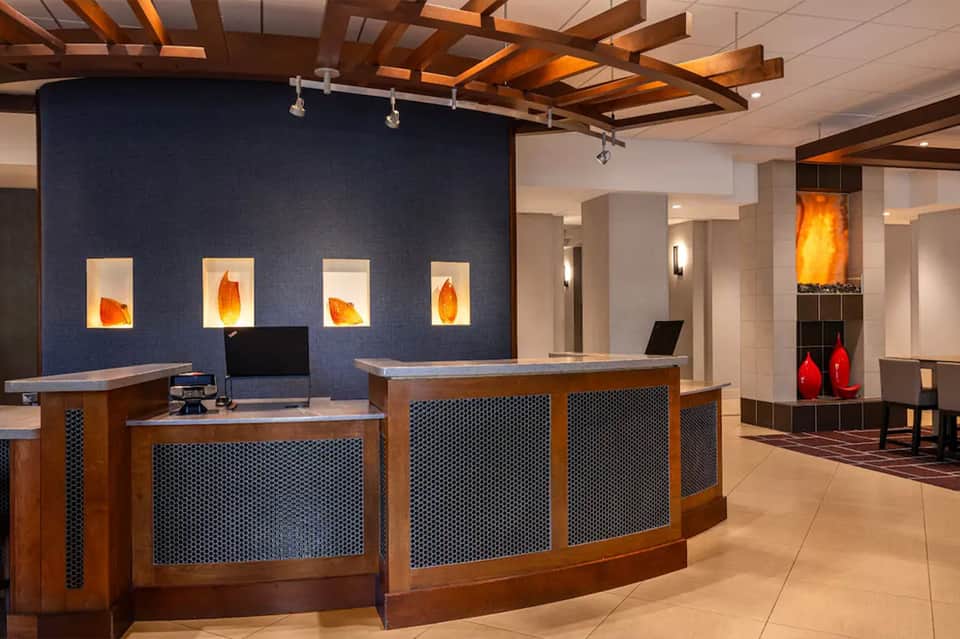 Modern hotel lobby with dual curved wooden reception desks, blue accent wall with artwork, and ambient lighting
