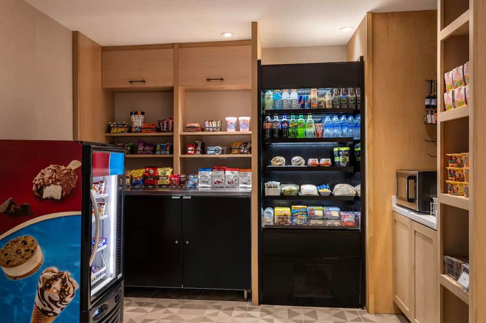 Modern resort snack bar with refrigerated beverage display, vending machines, and wooden cabinetry