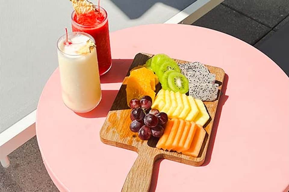 Pink table with fruit board and colorful beverages in tropical resort setting with ocean view