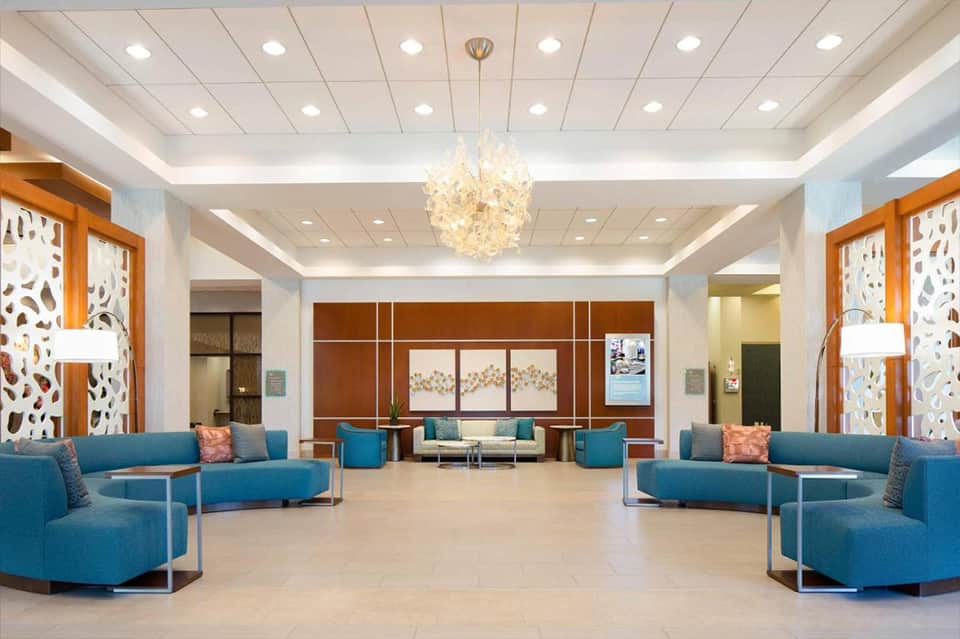 Modern hotel lobby with blue curved sofas, cream ceiling, glass pendant light, and decorative screens