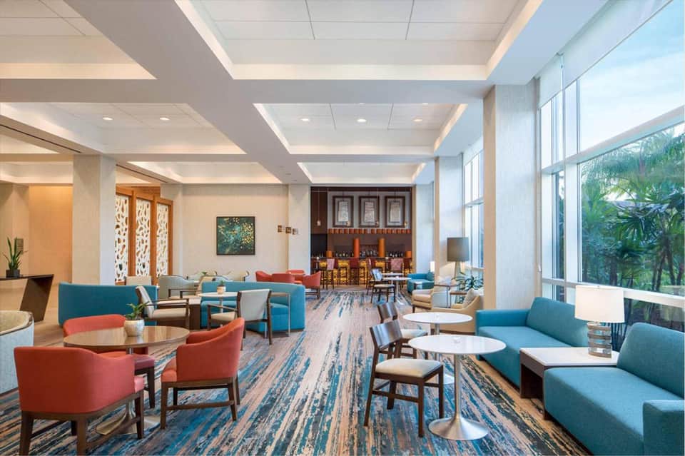 Spacious hotel lounge with blue and coral seating, patterned carpet, coffered ceiling, and views to bar area