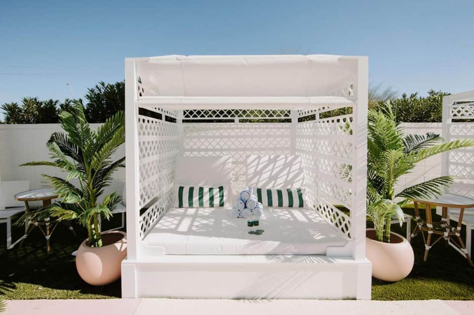 Luxury outdoor canopy bed with white drapes and green striped cushions in tropical garden setting