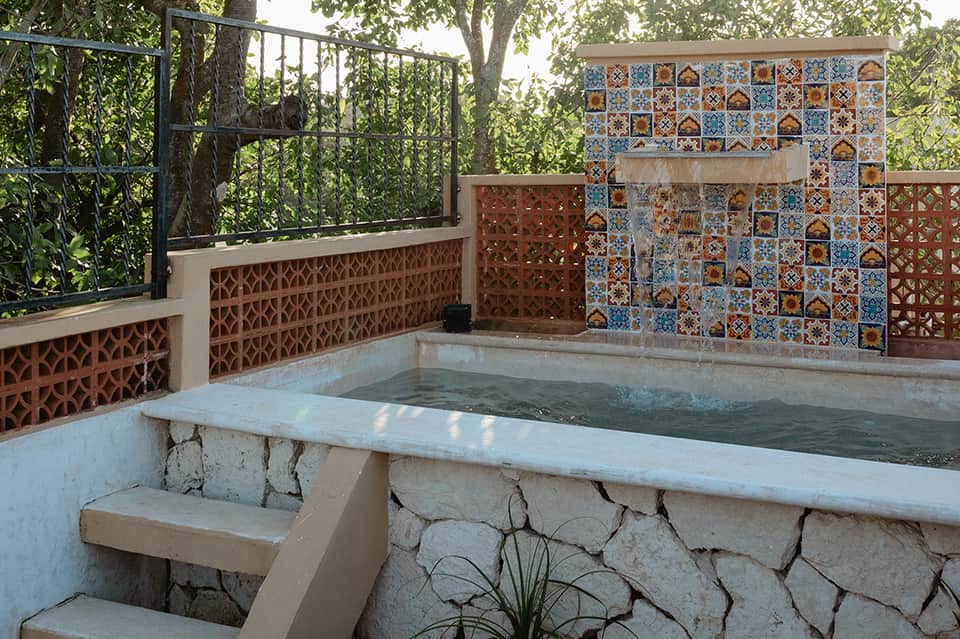 Outdoor hot tub with decorative tile walls, metal railings, and tree canopy