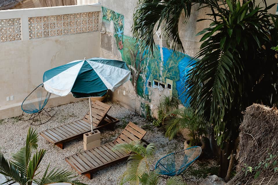 Intimate courtyard pool area with striped umbrella, wooden lounge chairs, and tropical plants