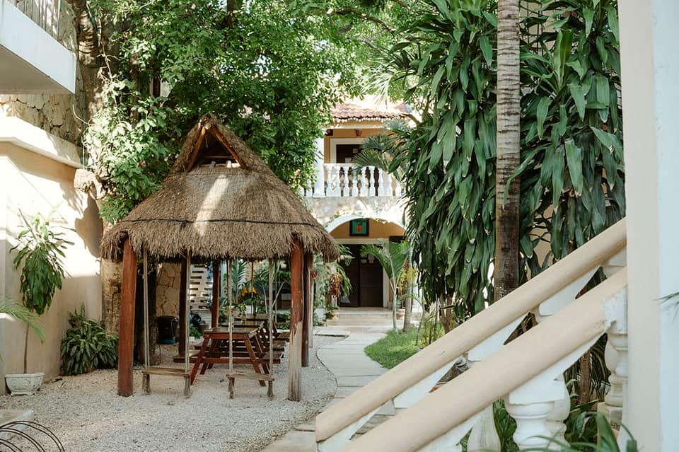 Tropical courtyard with thatched-roof gazebo, colonial architecture, and lush vegetation
