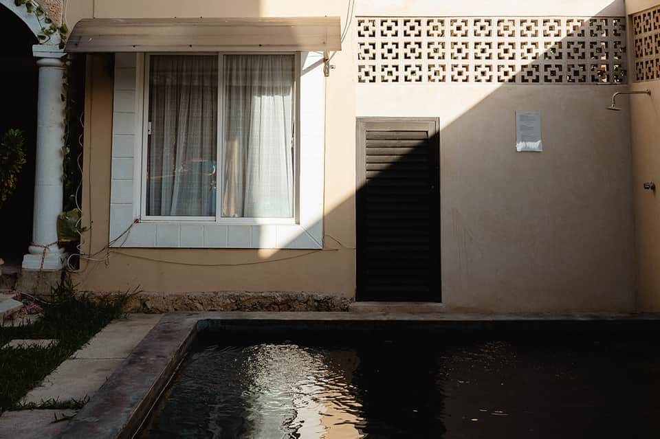 Minimalist residential patio with pool, large window, white curtains, decorative lattice wall panel, and natural sunlight