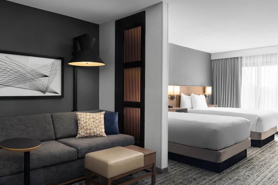 Modern hotel suite with gray sofa, bed visible through partition, and artistic wall decor