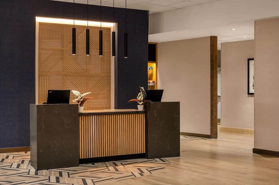 Contemporary hotel lobby featuring wooden accent wall, dark reception desk with pendant lighting