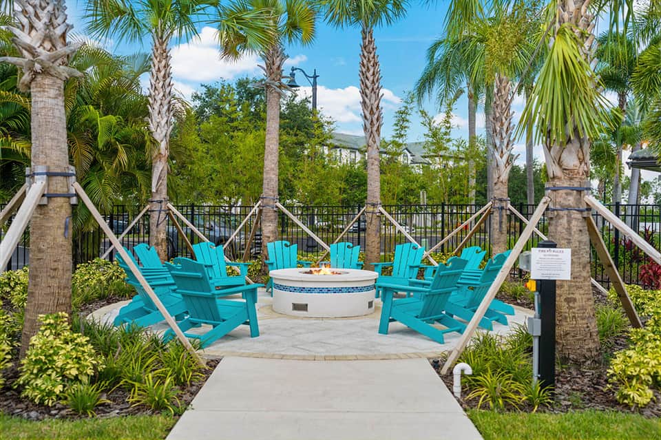 Poolside gathering spot with turquoise Adirondack chairs around fire pit under palm trees