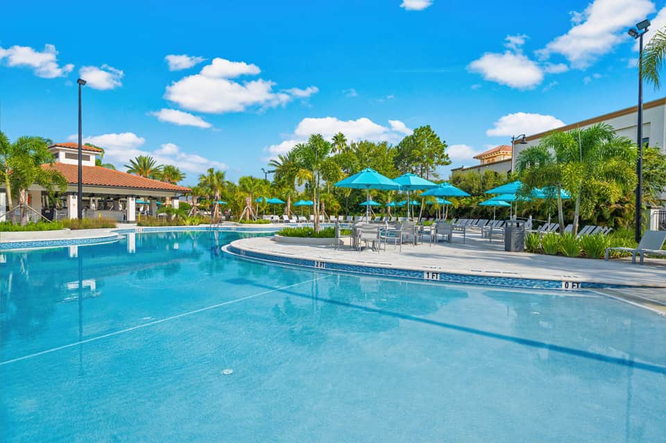 Outdoor pool with blue umbrellas, palm trees, cabanas, and recreational facilities