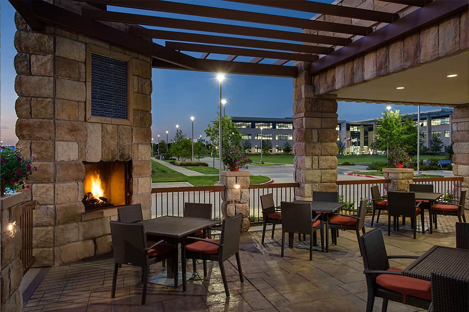 Outdoor patio with fireplace, seating area, and pergola at twilight with green lawn