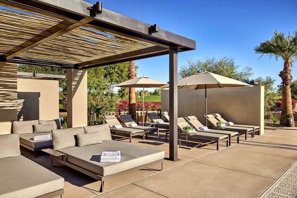 Modern resort patio with lounge seating, pergola shade structure, umbrellas, and manicured grounds