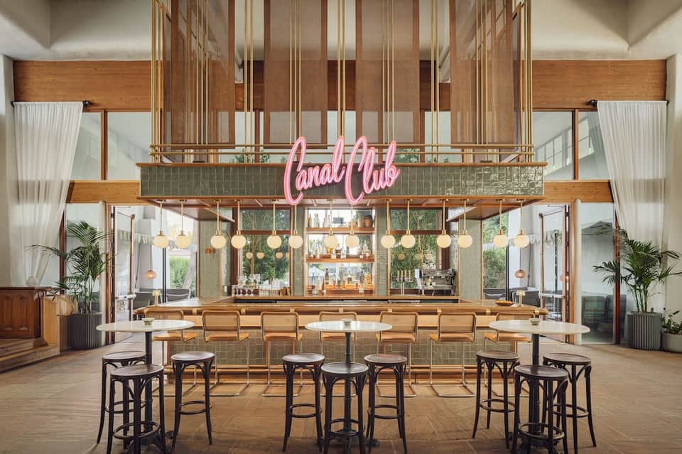 Modern bar interior with pink neon sign, wooden counter, pendant lights, and barstools