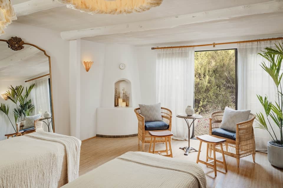 Spa resort room with twin beds, wicker chairs, and glass doors overlooking nature