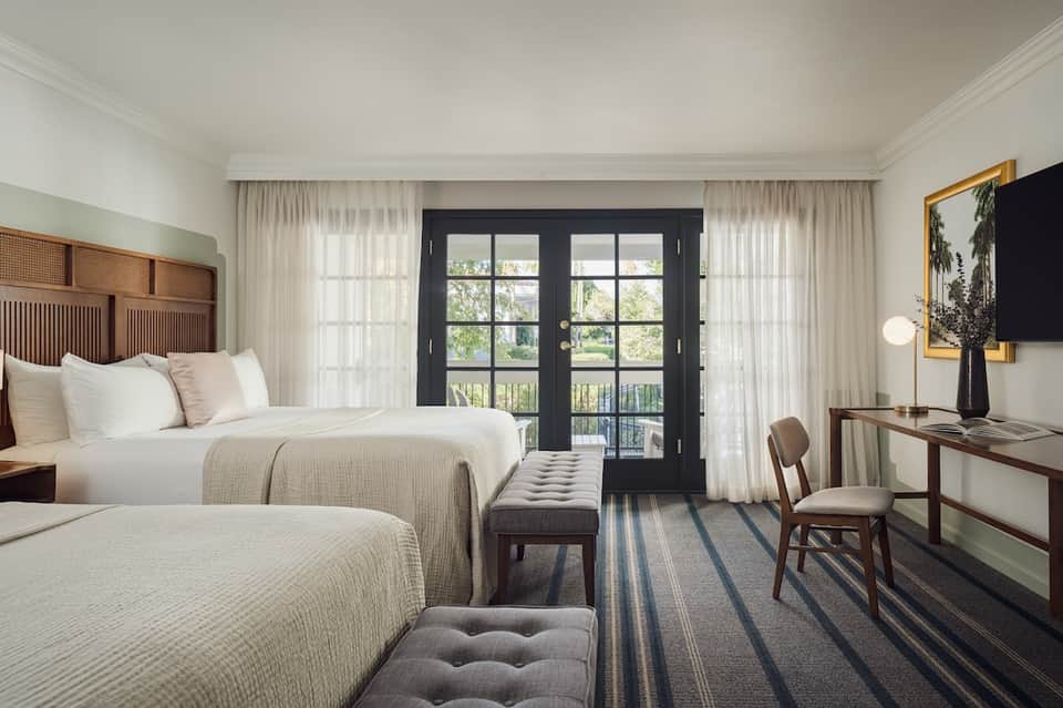 Hotel room with two queen beds, dark balcony doors, curtains, and mid-century modern furnishings