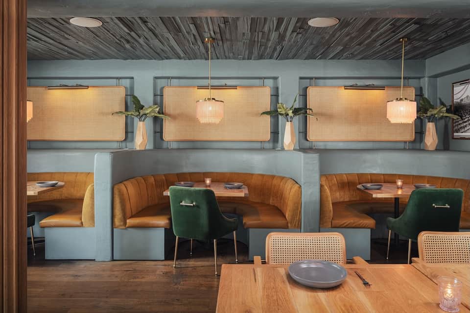 Contemporary restaurant dining area with orange velvet booths, woven wall panels, and pendant lighting