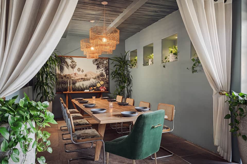 Upscale dining room with wooden table, modern chairs, pendant lighting, plants, and palm tree artwork