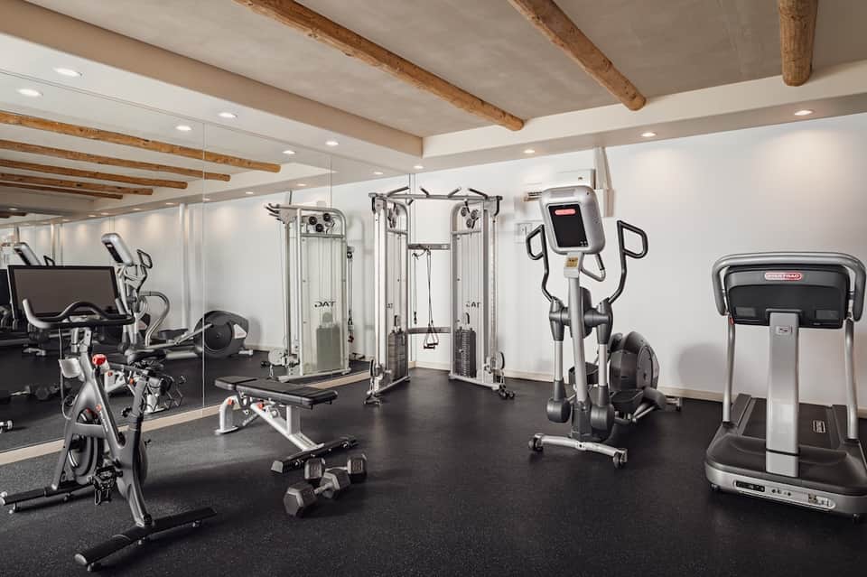 Upscale fitness center with cardio equipment, weight machines, wooden ceiling beams, and mirrors