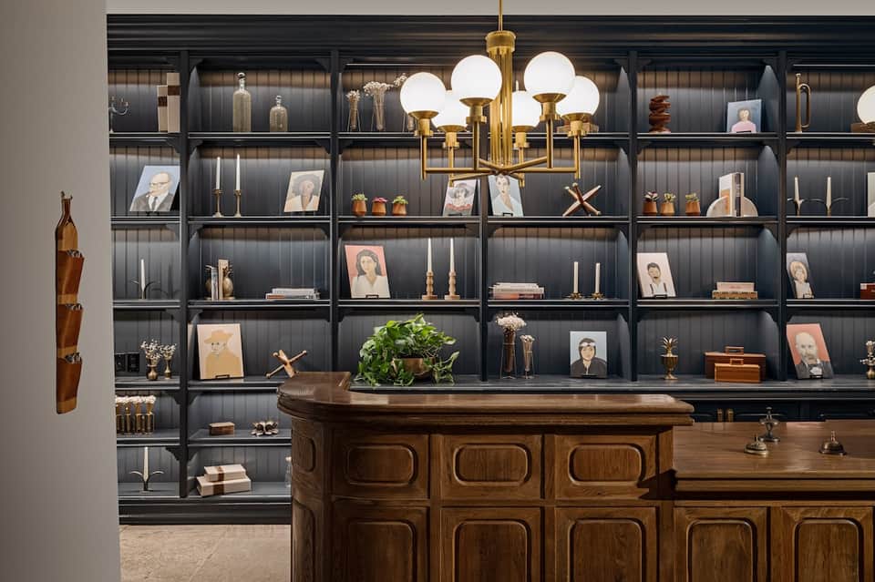 Elegant wood-paneled reception desk with brass chandelier and extensive curated shelving displaying artwork and decorative items.