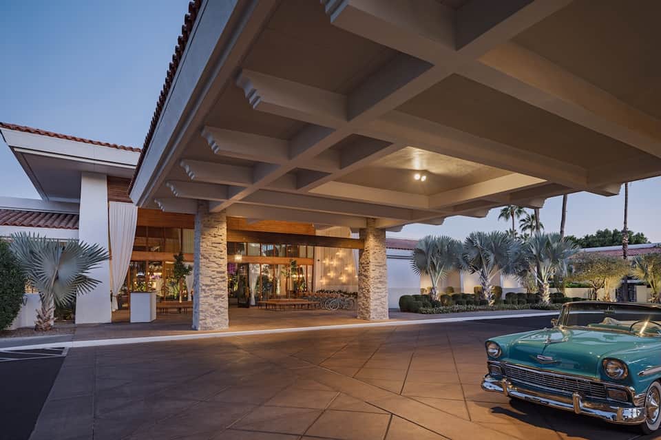Modern resort entrance with stone columns, flat roof, palm trees, and vintage turquoise car