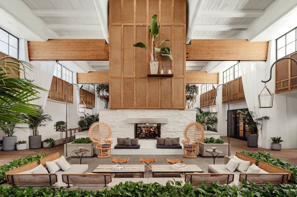Modern hotel lobby with wooden ceiling beams, fireplace, and tropical plants