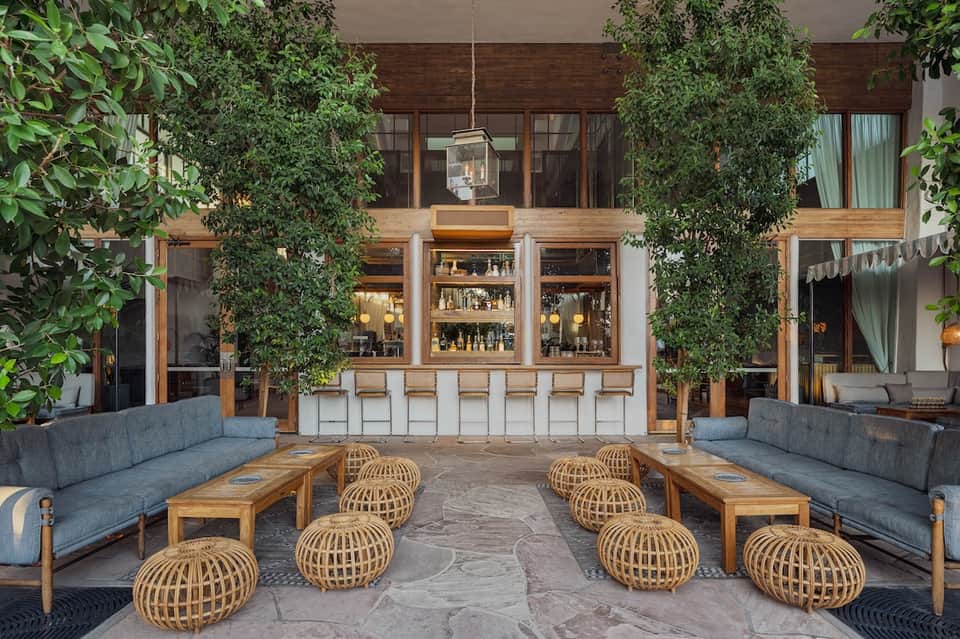 Contemporary courtyard bar with ivy-covered wooden bar, gray seating, and decorative woven poufs