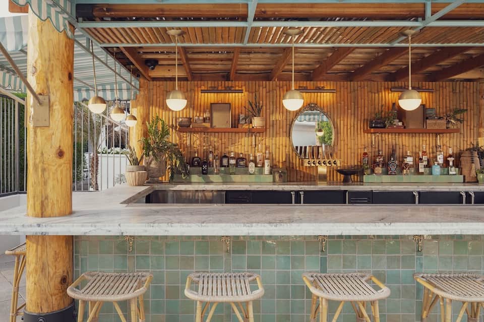 Modern wooden bar counter with pendant lights, potted plants, and shelved bottles