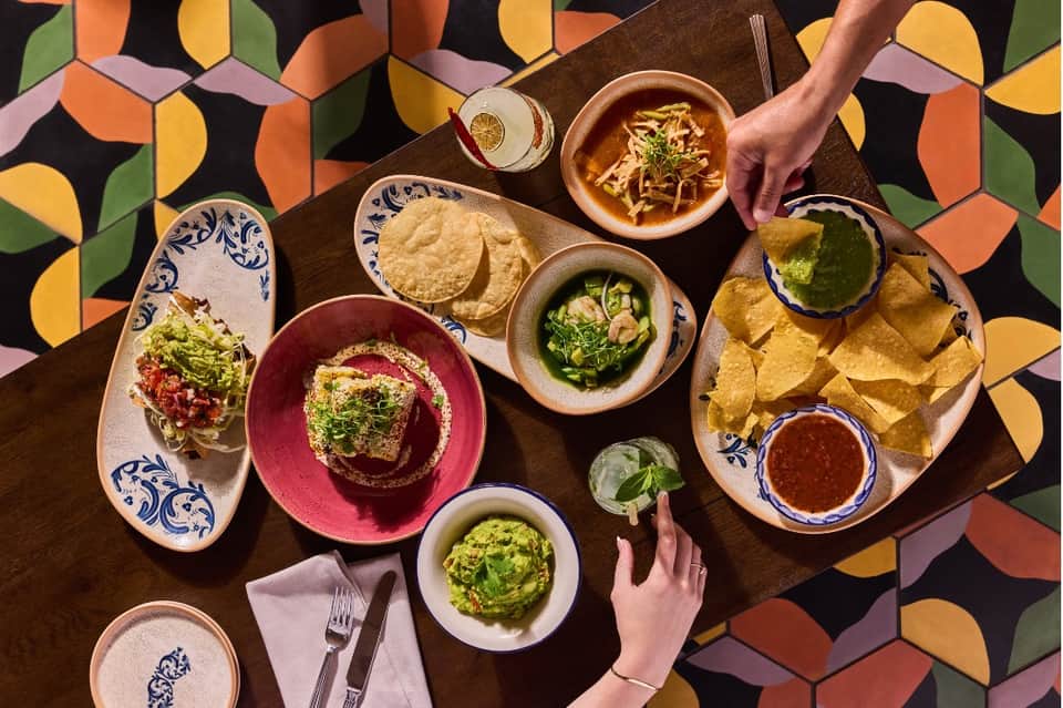 Colorful restaurant table with Mexican cuisine, guacamole, tacos, salsa, and chips overhead view
