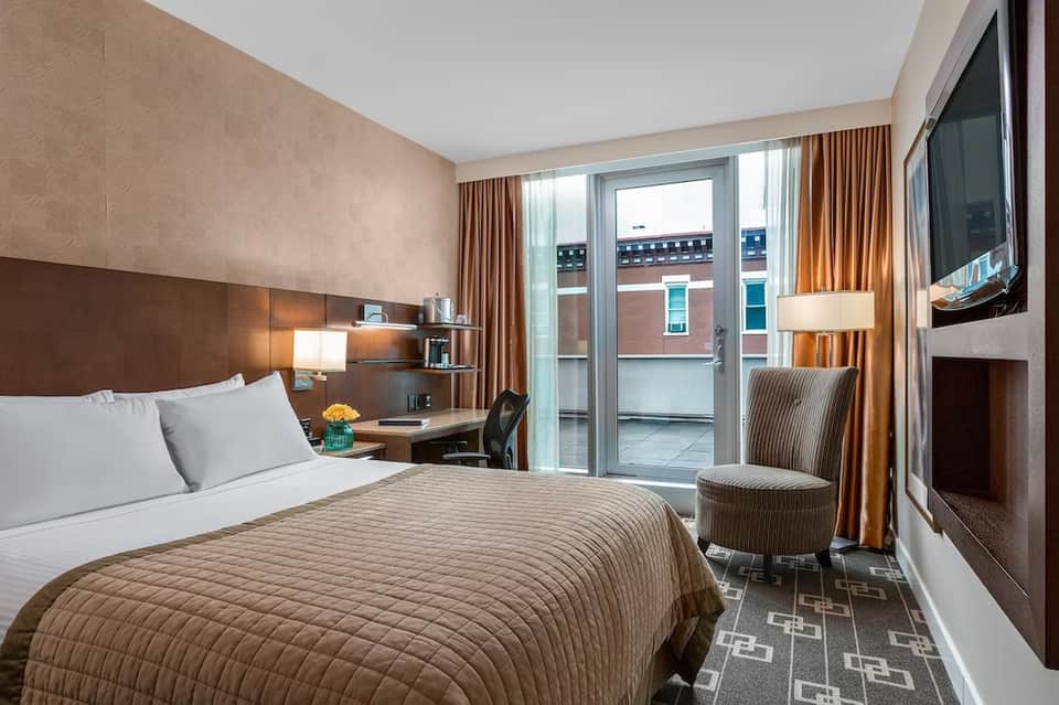 Contemporary hotel bedroom with brown bedding, terrace view, and flat-screen TV