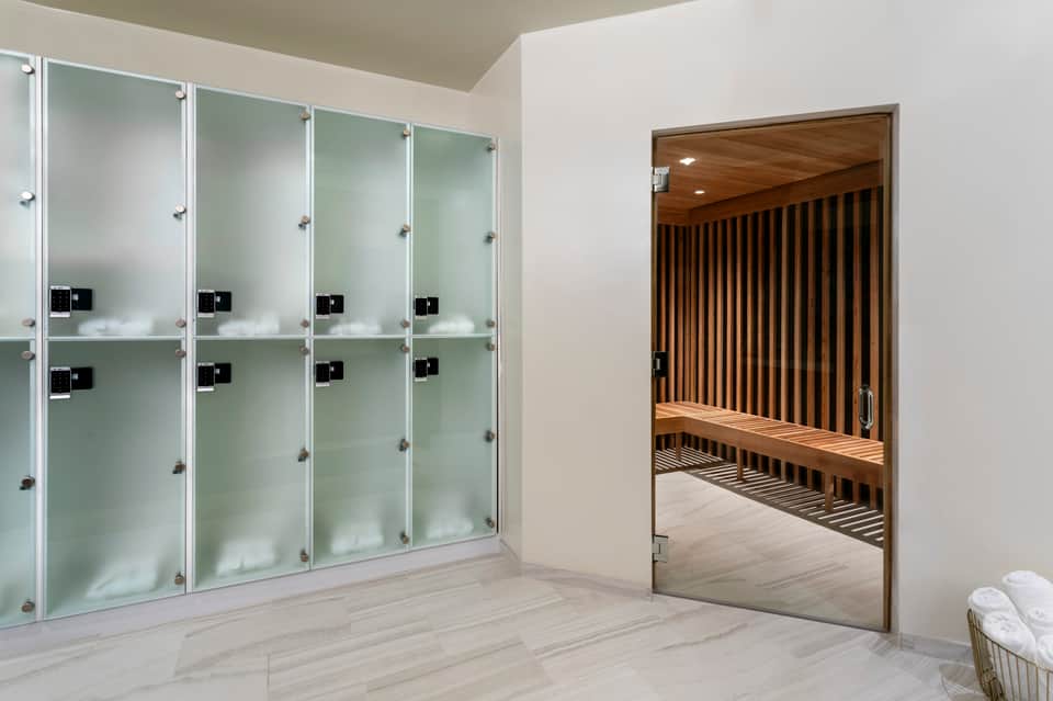 Modern spa locker room with glass lockers and wooden sauna room entrance