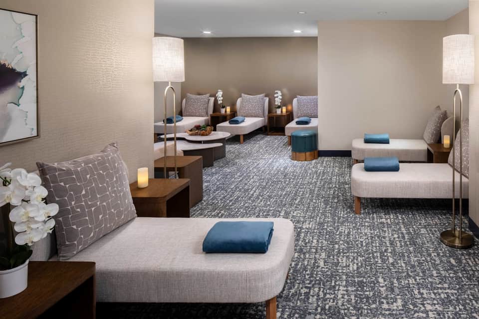 Spa relaxation room with multiple lounge chairs, soft lighting, white orchid decor, and calming neutral tones