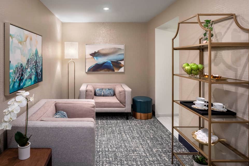 Modern hotel lounge with beige sectional sofa, abstract wall art, and metal shelving unit