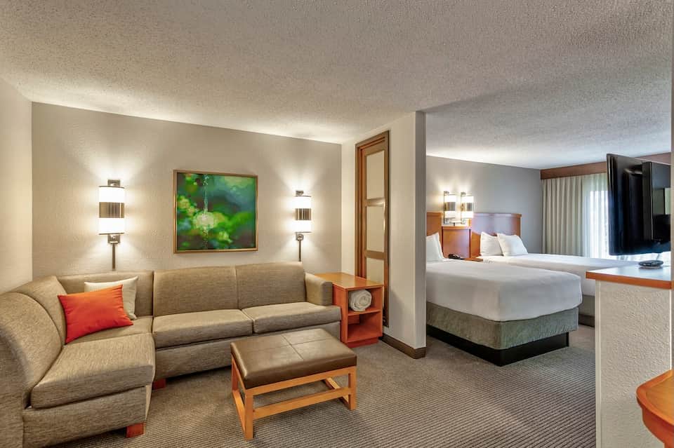 Spacious hotel suite with living area, sofa, and bedroom with white linens visible