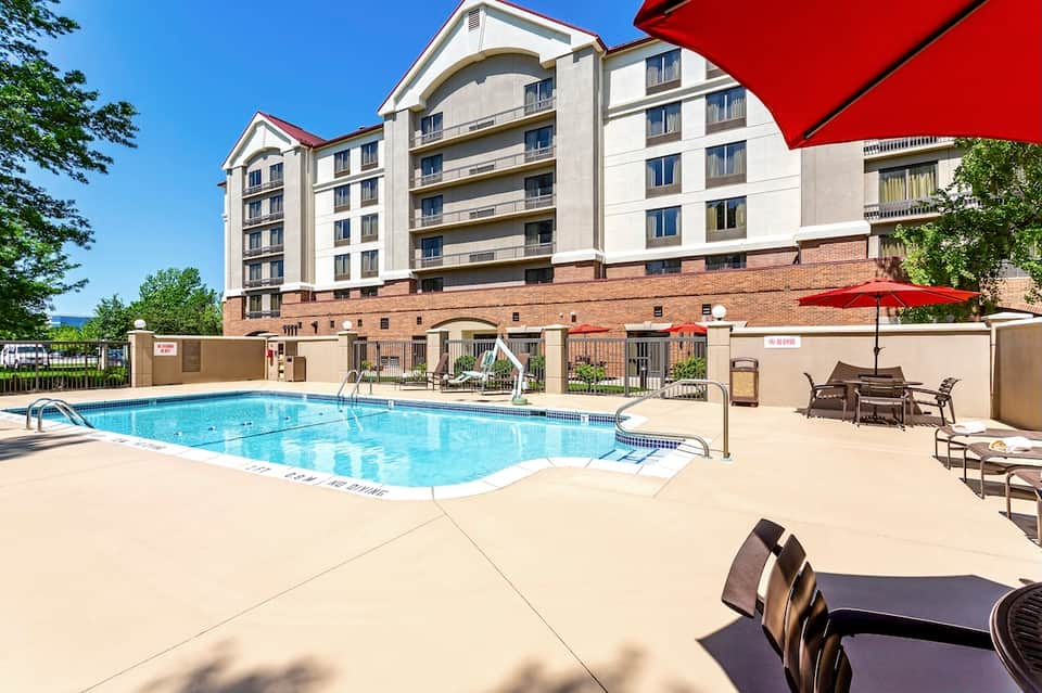 Outdoor swimming pool with red umbrellas, multi-story residential building, and landscaped patio area