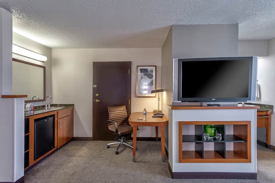 Hotel suite with kitchenette, desk area, TV, and wood furnishings