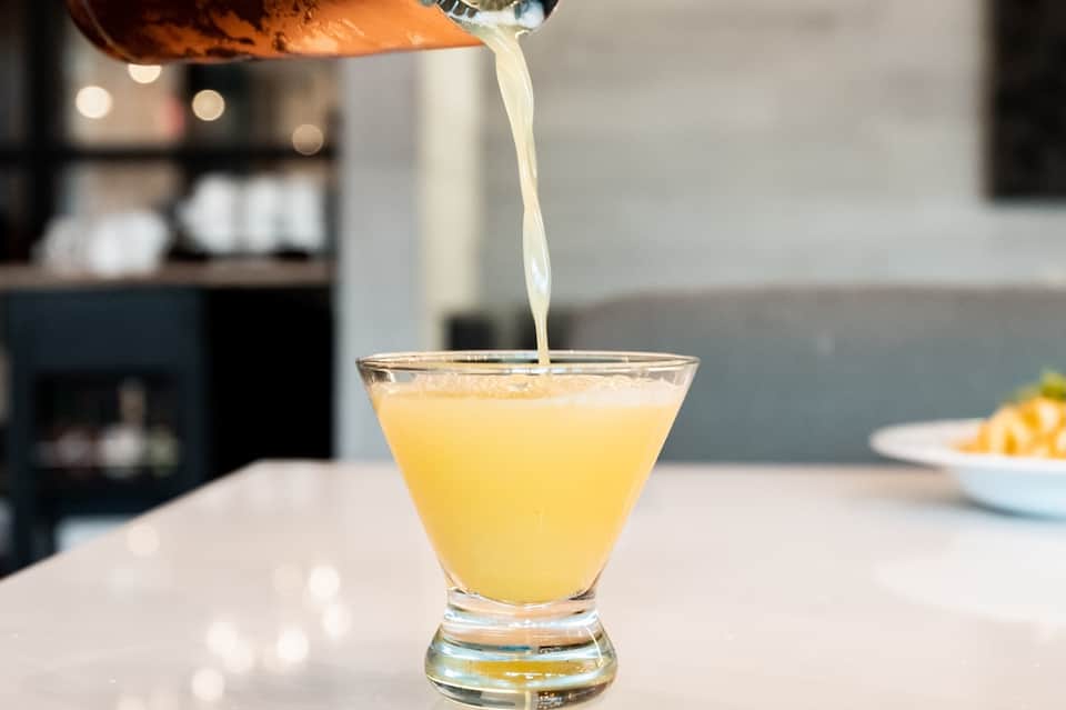 Bartender pouring a yellow cocktail into a glass at a hotel bar counter