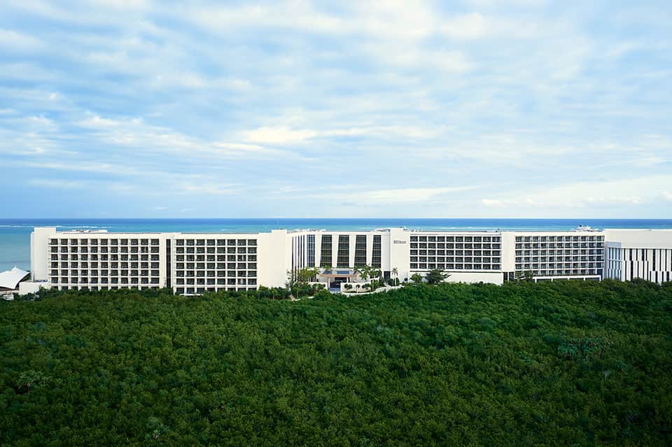 Modern Hilton hotel complex overlooking ocean with white buildings and surrounding tropical forest