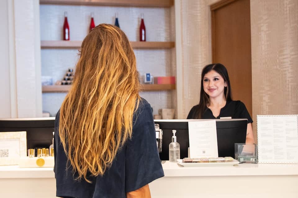 Woman with long auburn hair at hotel spa reception desk with staff member