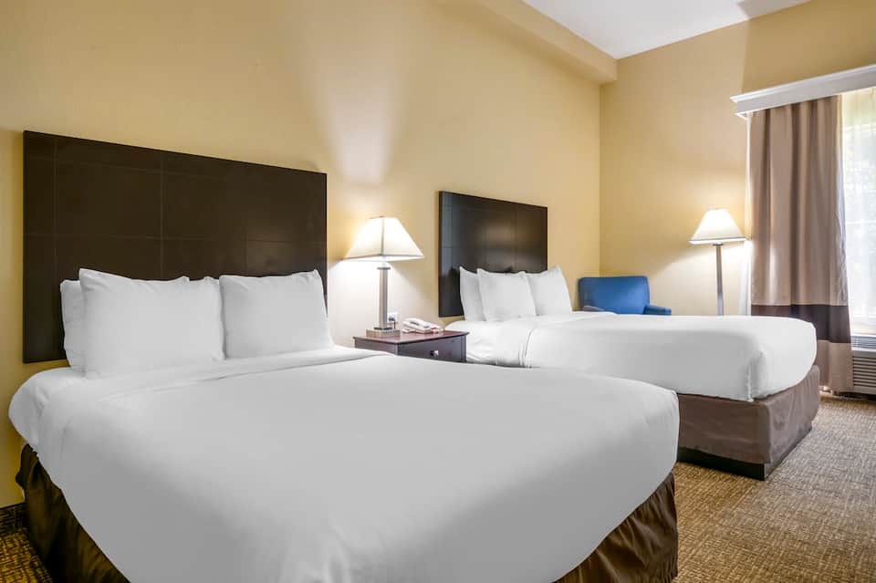 Hotel room with two queen beds, dark headboards, yellow walls, and modern furnishings