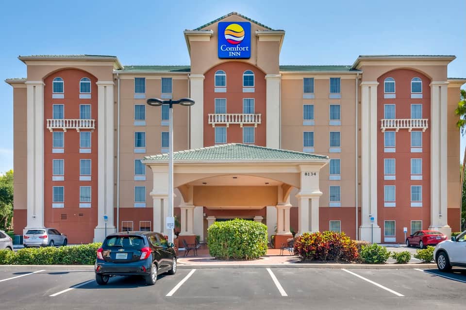 Comfort Inn hotel exterior with red and tan facade, white columns, green roof, parking lot entrance
