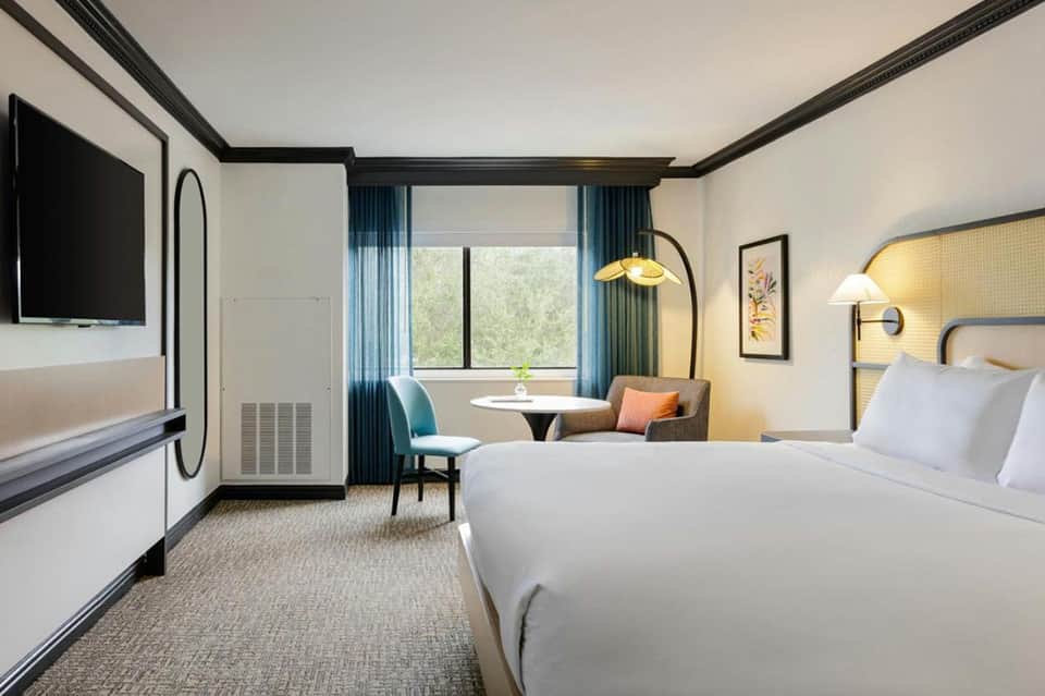 Modern hotel bedroom with dual queen beds, sitting area, and flat-screen TV
