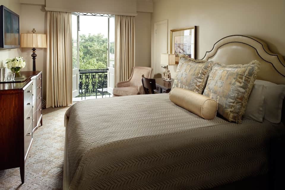 Luxury hotel bedroom with king bed, balcony doors, neutral tones, and elegant furnishings