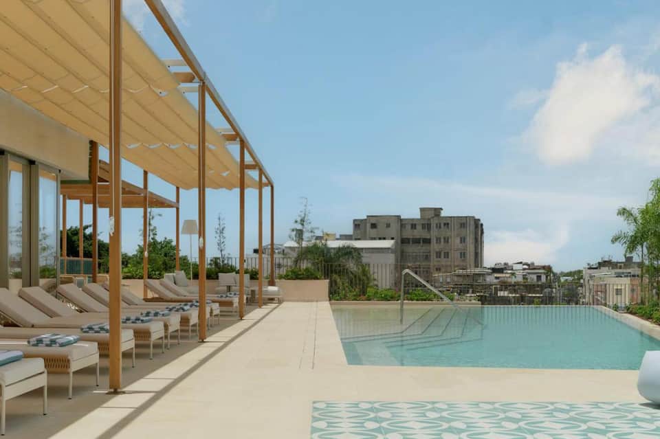 Modern rooftop pool with wooden pergola, lounge chairs, and city skyline views