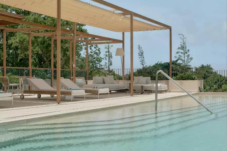 Modern poolside terrace with wooden pergola, lounge seating, and infinity pool overlooking landscaped gardens