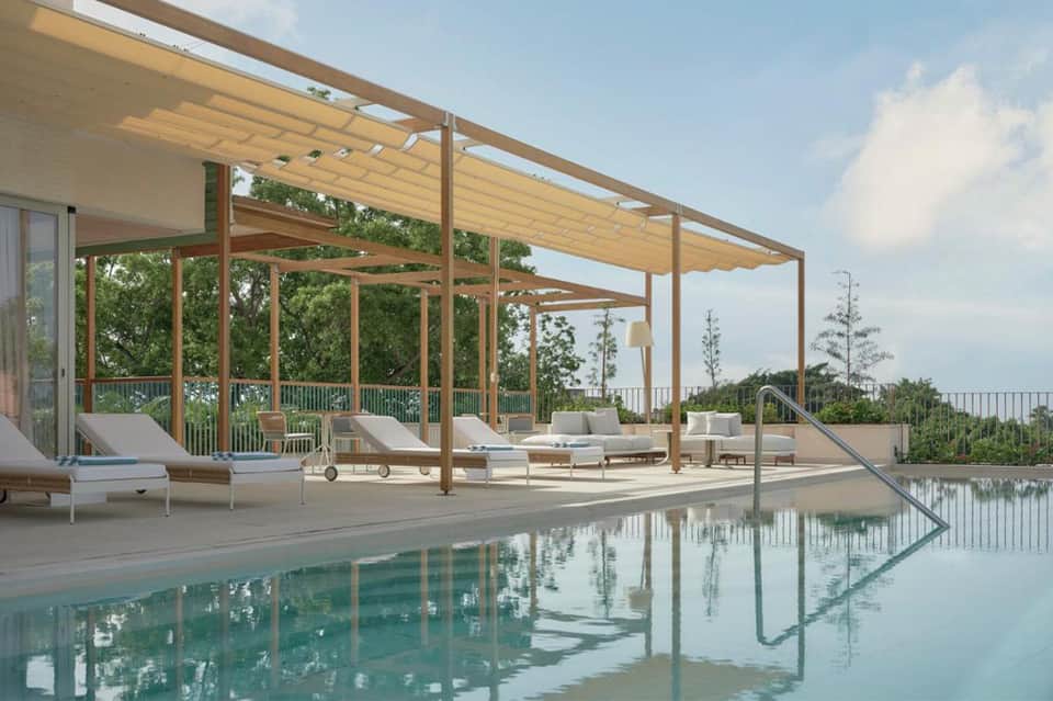 Luxury rooftop pool deck with wooden pergola, white lounge chairs, and scenic water views