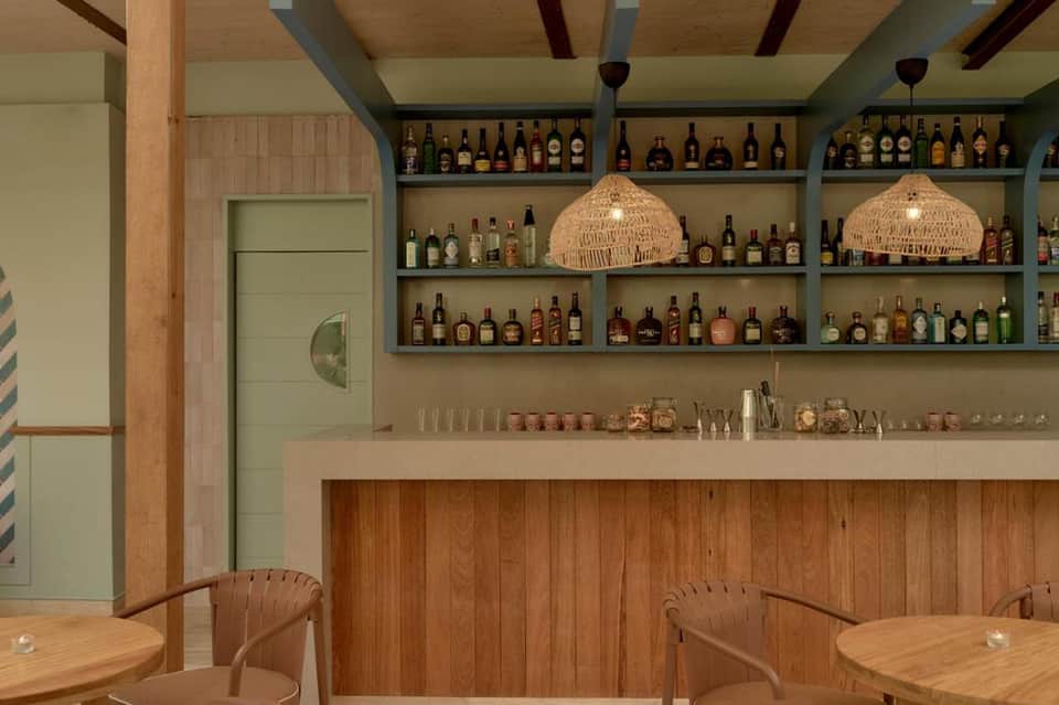 Upscale bar interior with wooden shelving displaying bottles, woven pendant lights, and wooden tables
