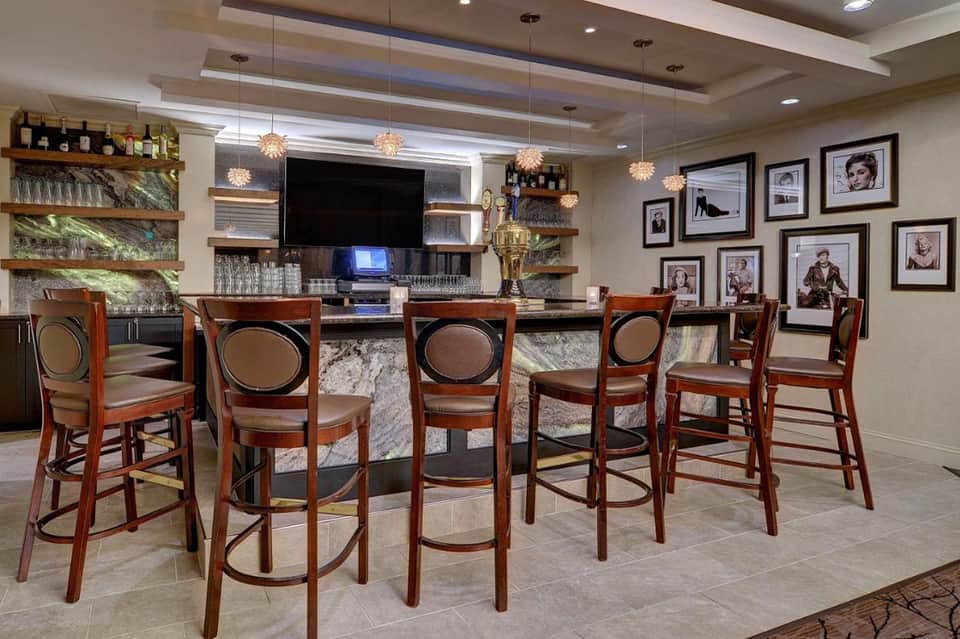 Upscale bar lounge with high seating, flat-screen TV, shelving with bottles, and framed artwork