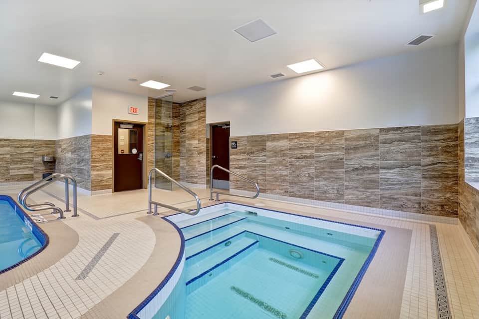 Indoor spa area with hot tubs, stone tile walls, and handrails for accessibility