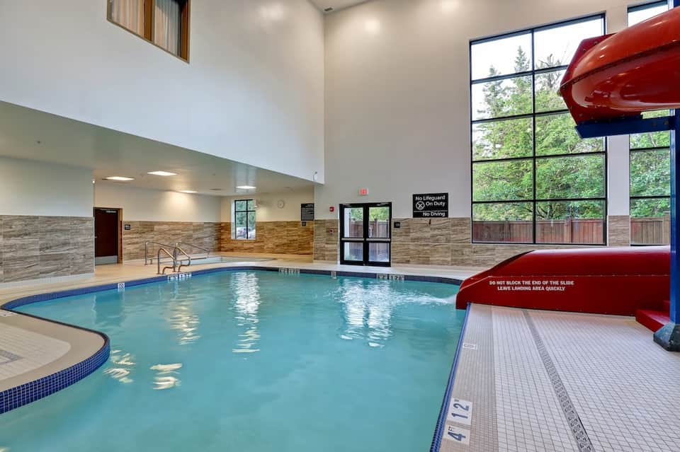 Indoor swimming pool with water slide, modern ceiling, wood accents, and large windows